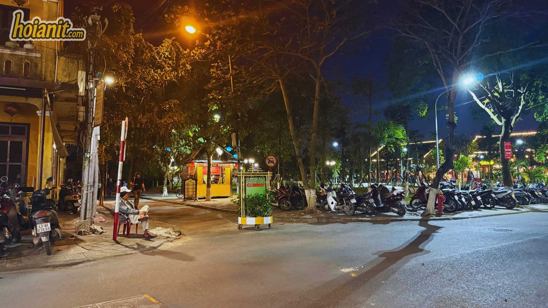 Scooters lined up along the kerb at night on the edge of the Hoi An bike parking zone