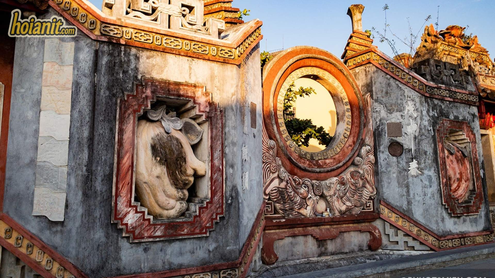 Cận cảnh phù điêu vữa đắp và ô cửa tròn trên tam quan chùa Bà Mụ Hội An lúc nắng chiều