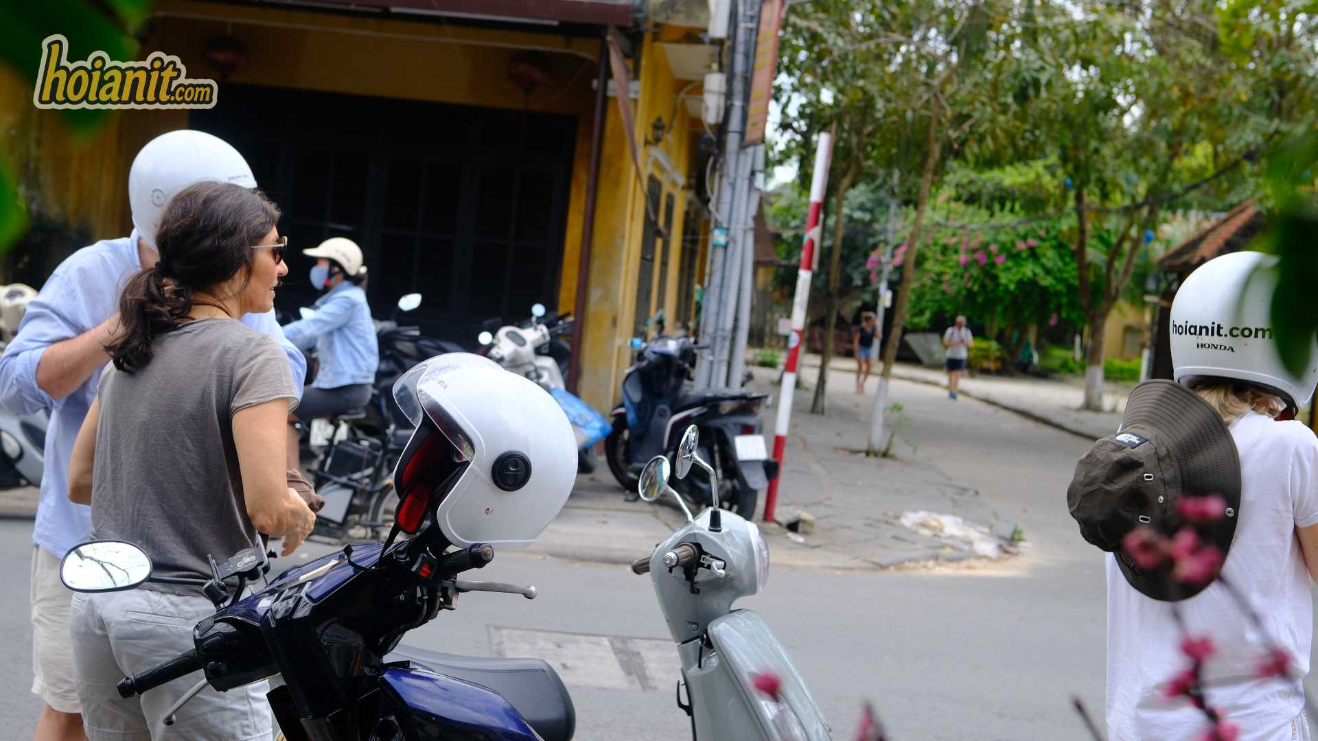 Hoi An Motorbike Rental Price 20261 Rider trying on a helmet beside a blue scooter, helmets included in the daily rate