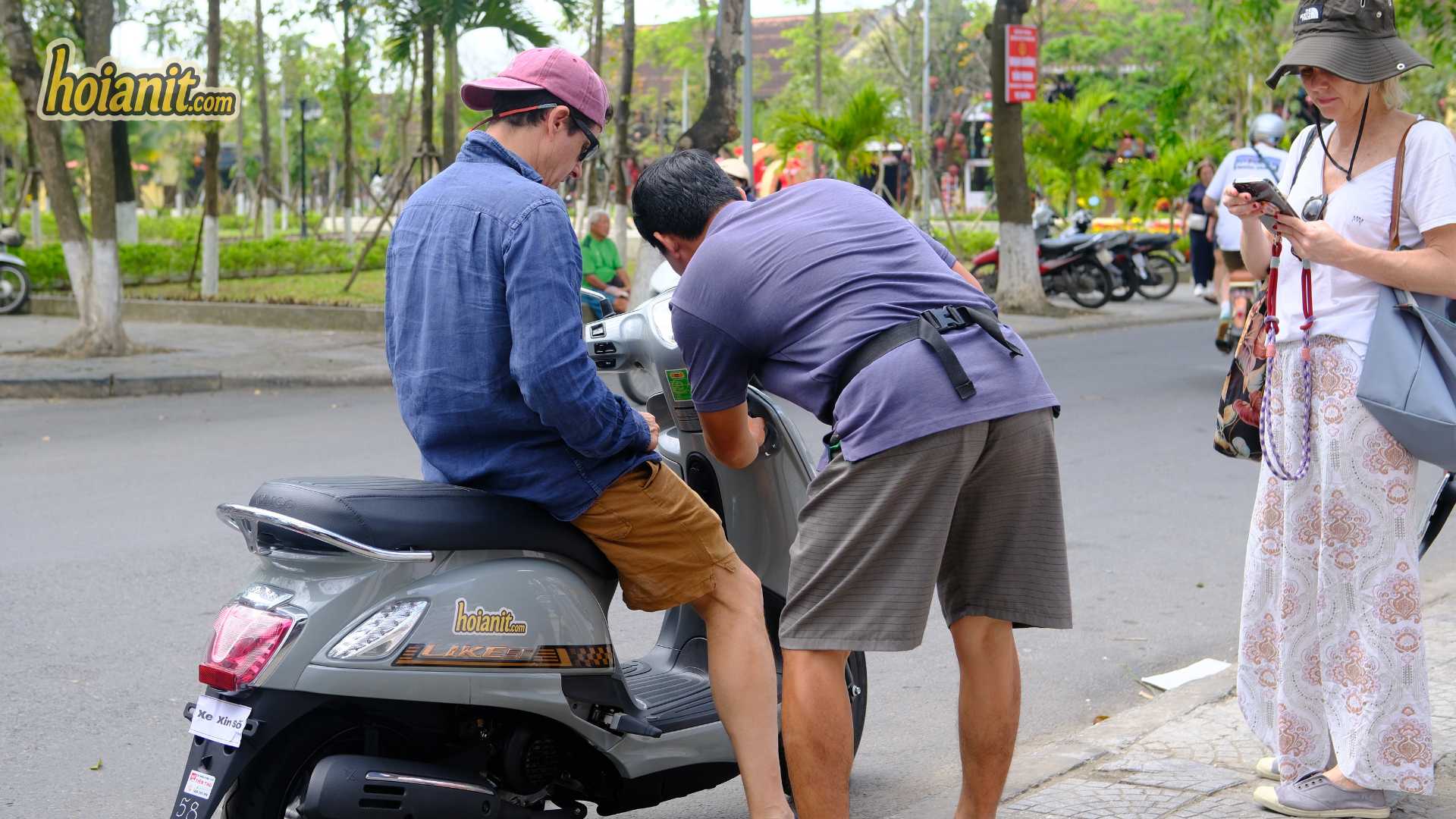Hoi An Motorbike Rental Price 20262 Motorbike rental Hoi An price check at handover: staff and a customer looking over a grey scooter