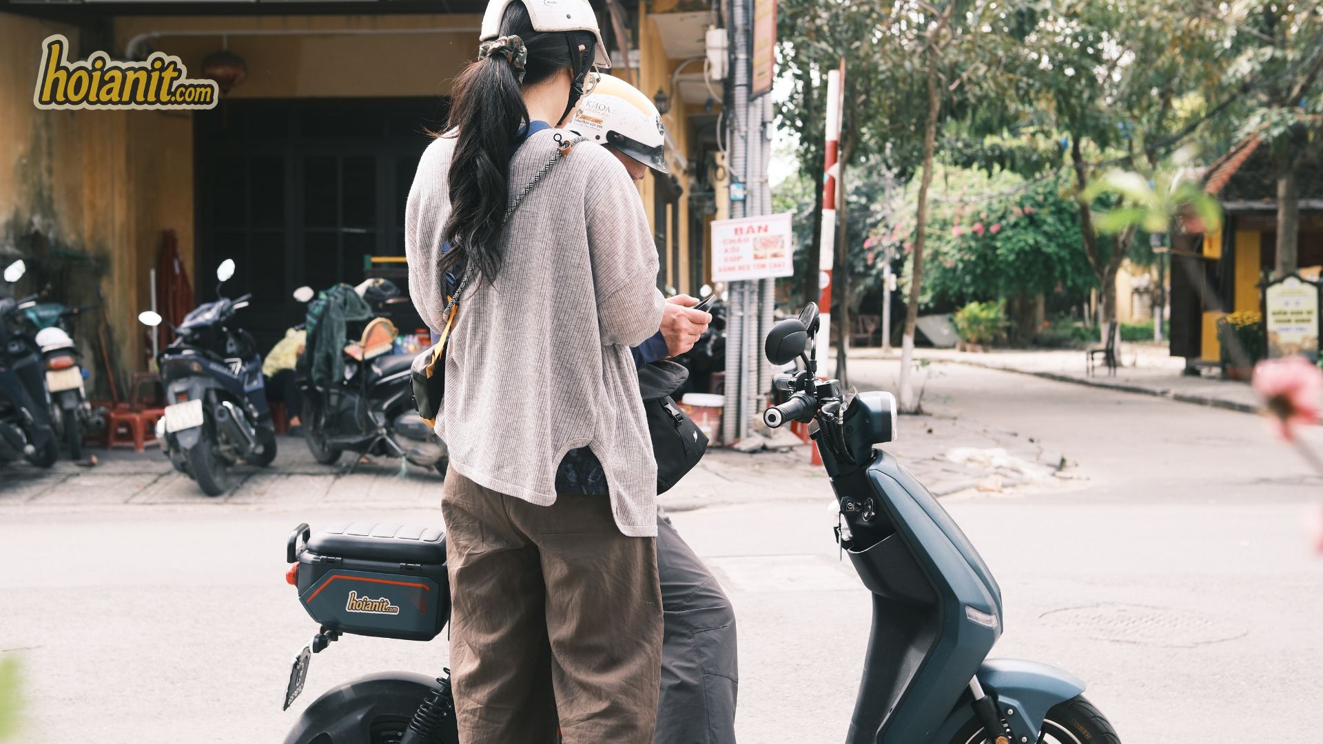 Motorbike Rental Hoi An Price3 Rider in a helmet beside a dark scooter on a quiet Hoi An street before setting off