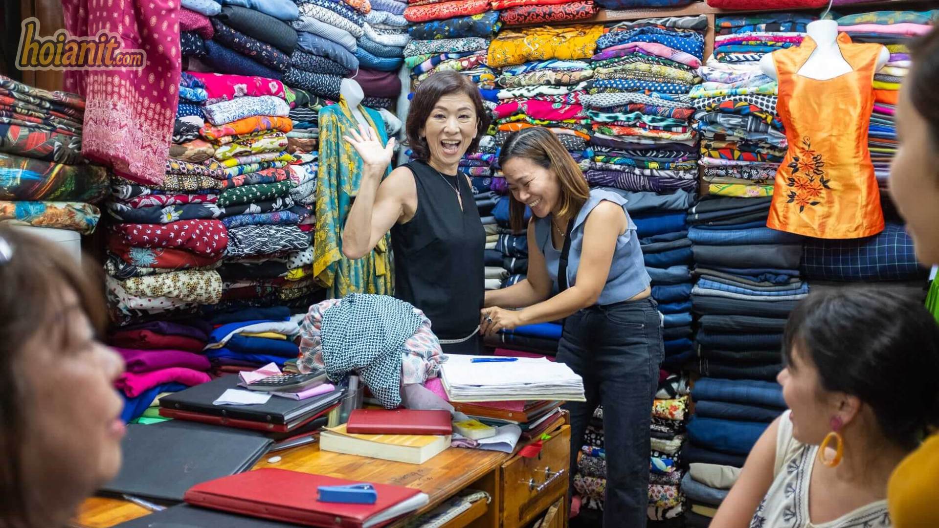 Finished custom suits and shirts hanging at a Hoi An tailor shop, showing 2026 price ranges