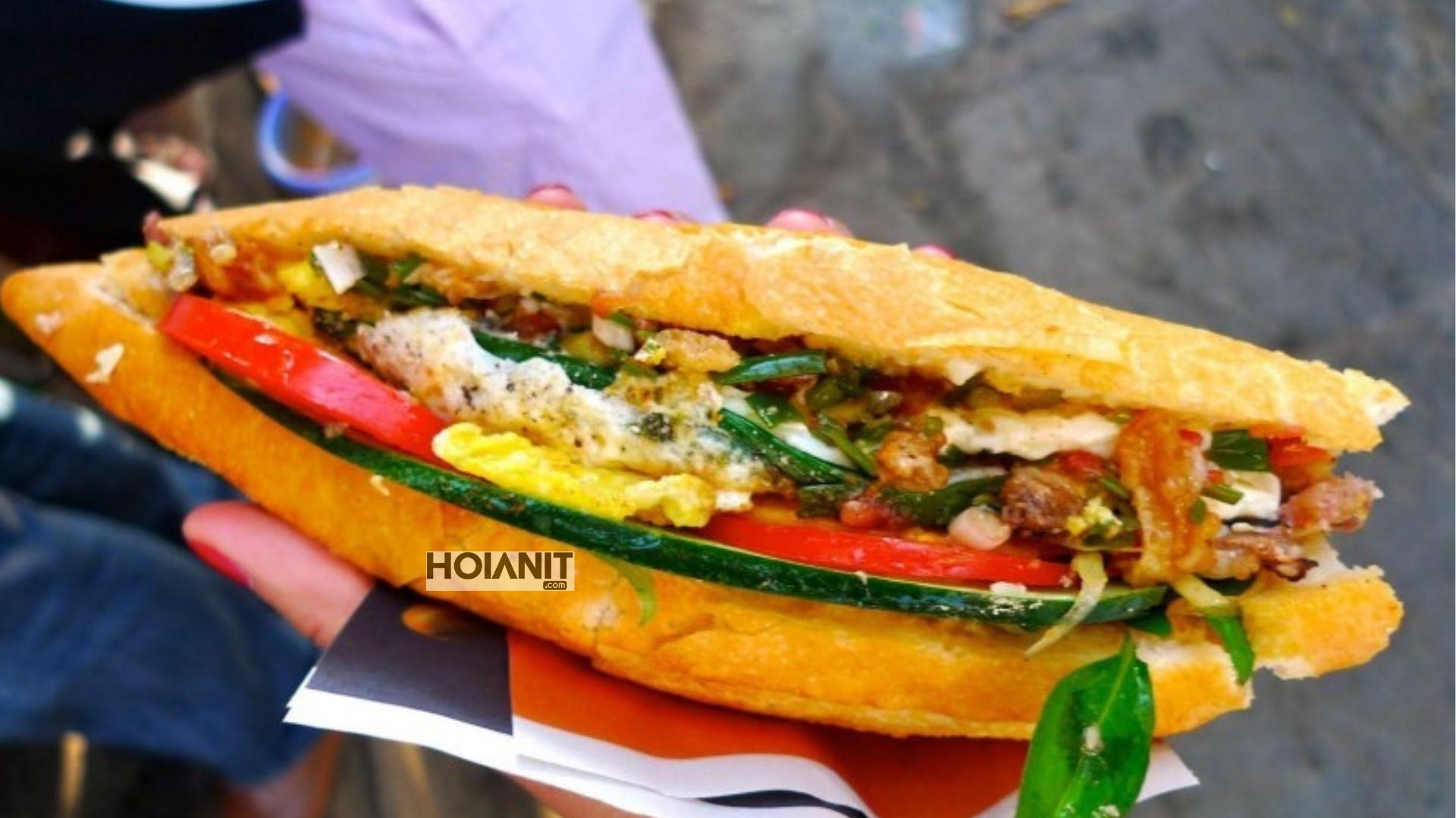 Hoi An banh mi filled with egg, cold cuts, herbs and cucumber held in hand