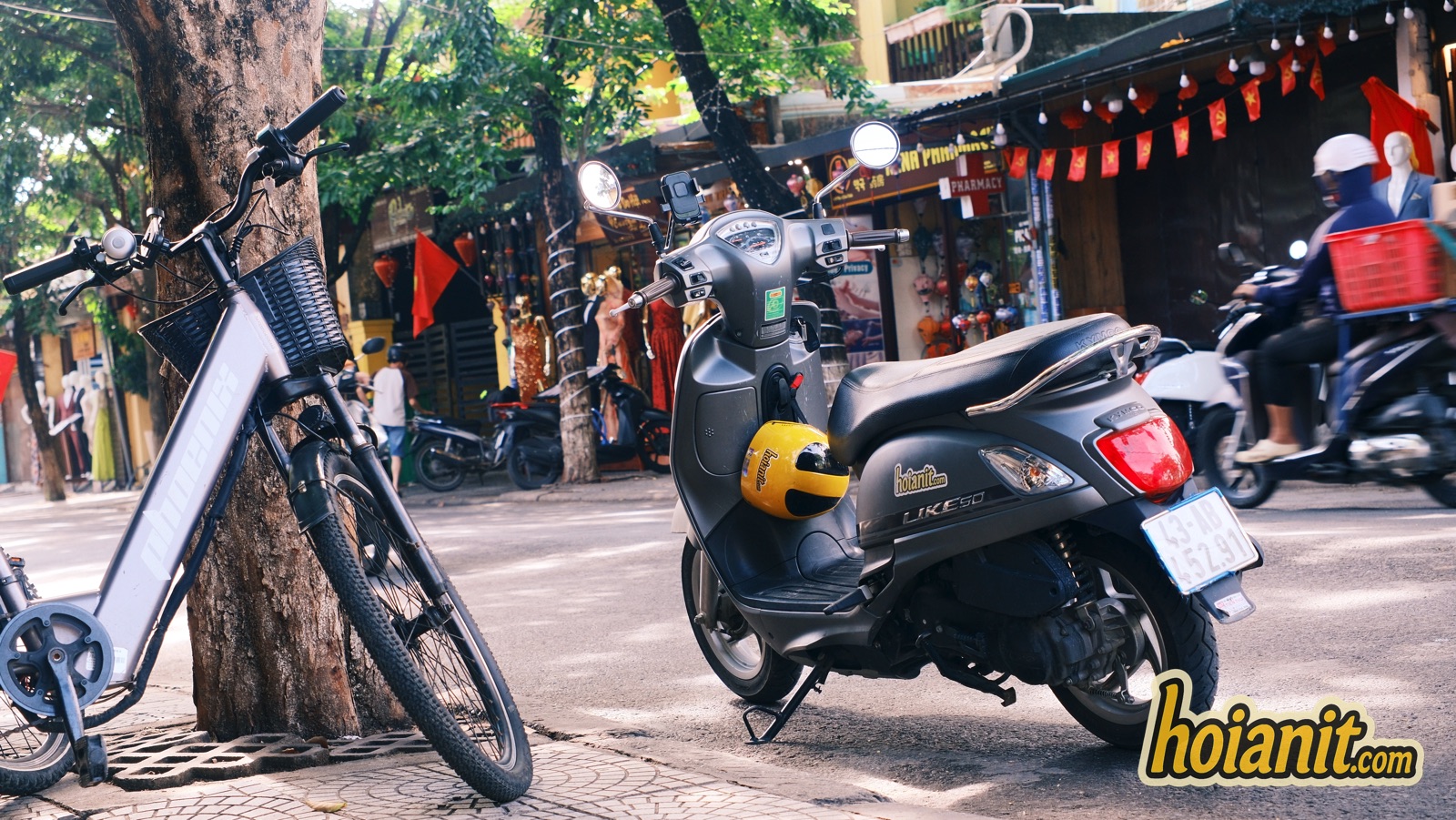 KYMCO Like 50 scooter with a yellow helmet beside an electric bicycle on a Hoi An Old Town street