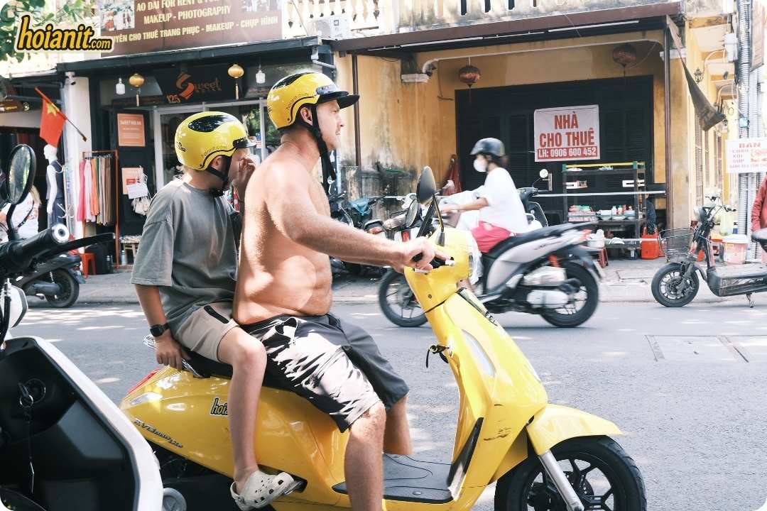 Two riders in yellow helmets on scooters heading out of Hoi An for a day ride