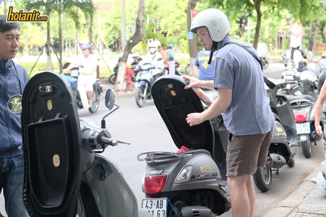 Rider in a helmet checking the under-seat storage of a KYMCO Like scooter during a Hoi An scooter rental handover