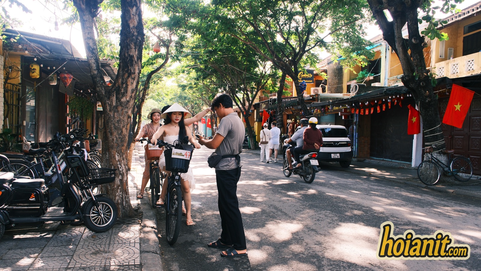 Hoi An Old Town street with lanterns, flags, a woman on a bicycle and parked electric bikes