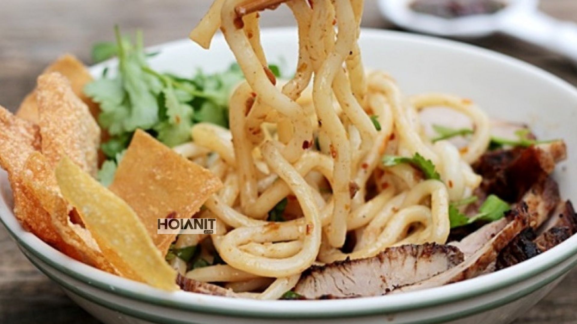 Thick cao lau noodles lifted with chopsticks showing their square-cut shape