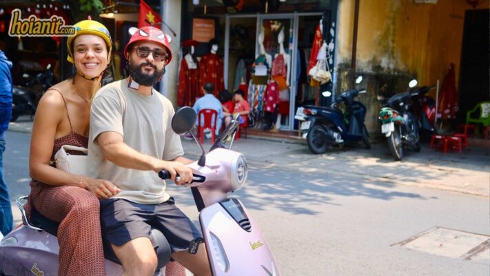 Couple riding VinFast evo pink scooter Hoi An old town smiling