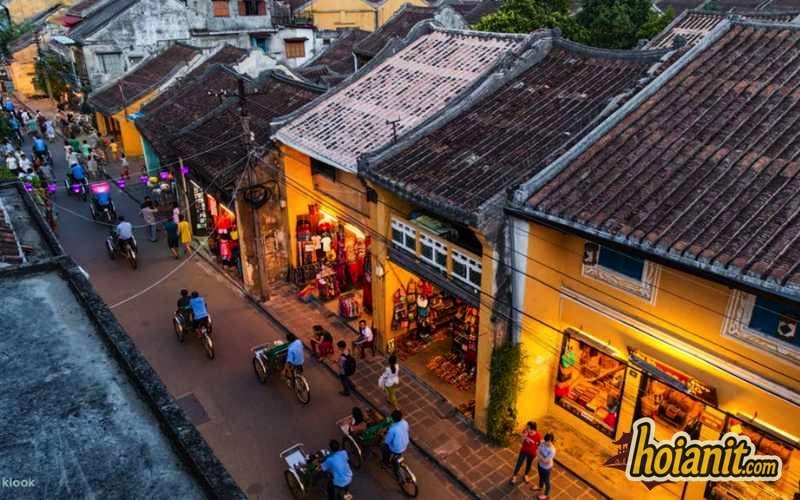 Cyclos and pedestrians on a yellow-walled street in Hoi An Ancient Town seen from above