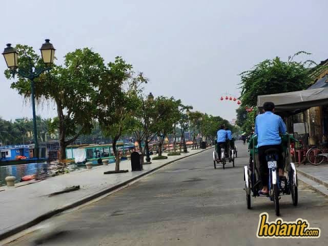 Two cyclos carrying passengers along the Thu Bon riverside road in Hoi An at dusk
