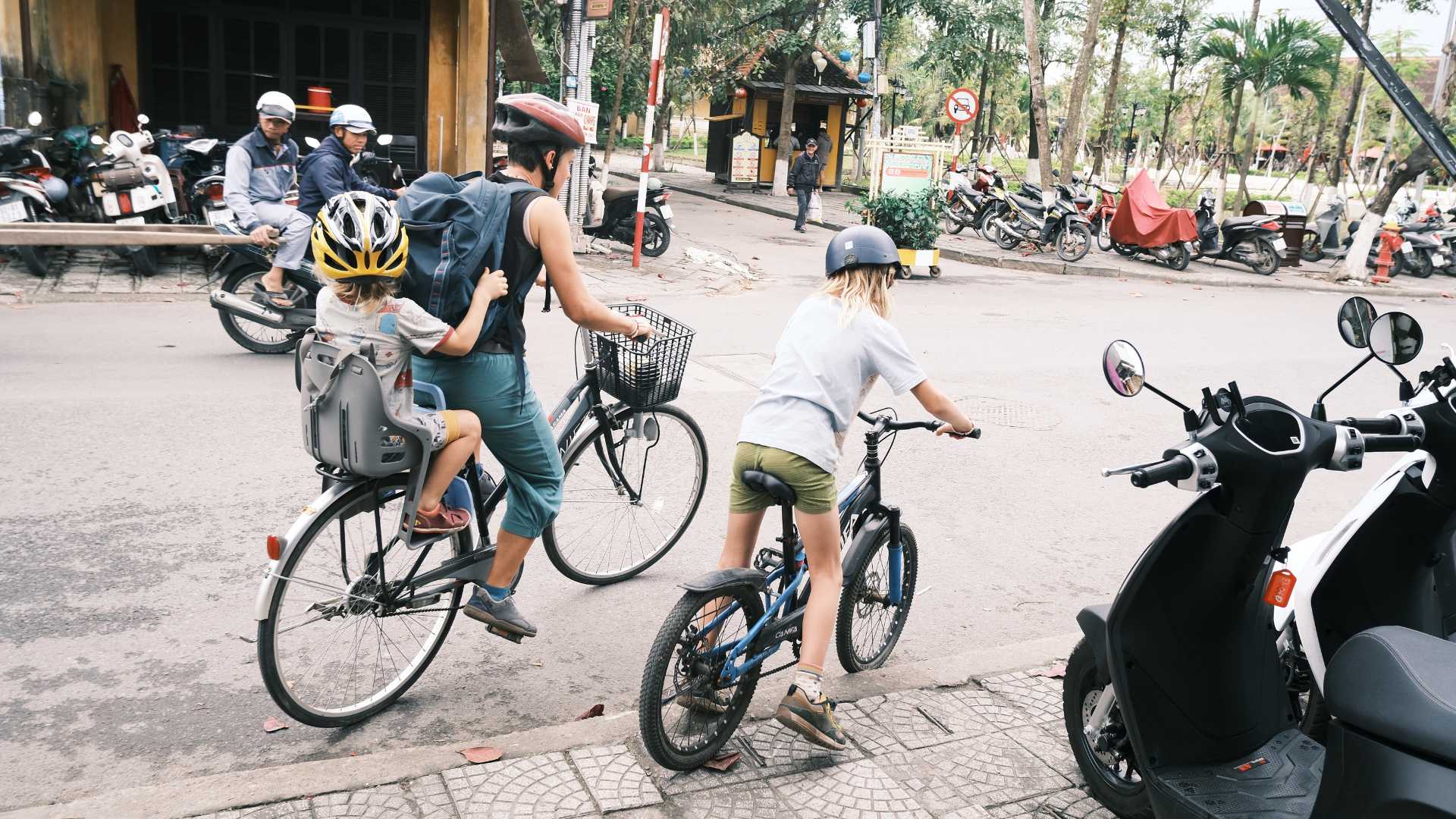 family riding bicycles hoi an park child seat kids Family cycling in Hoi An with a toddler in a child seat and an older child on a kids' bike