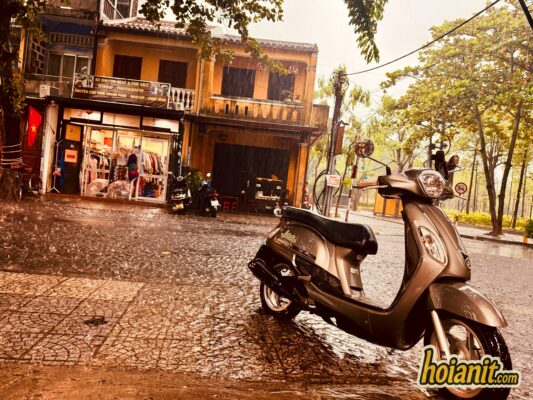 Scooter parked on a wet street in front of yellow shophouses in Hoi An