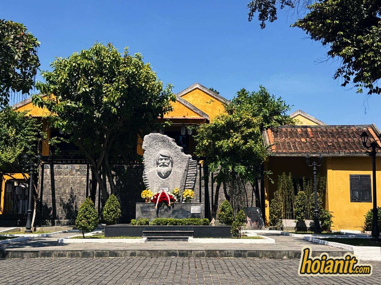Kazik Hoi An monument among trees and yellow heritage houses in the park on Tran Phu Street