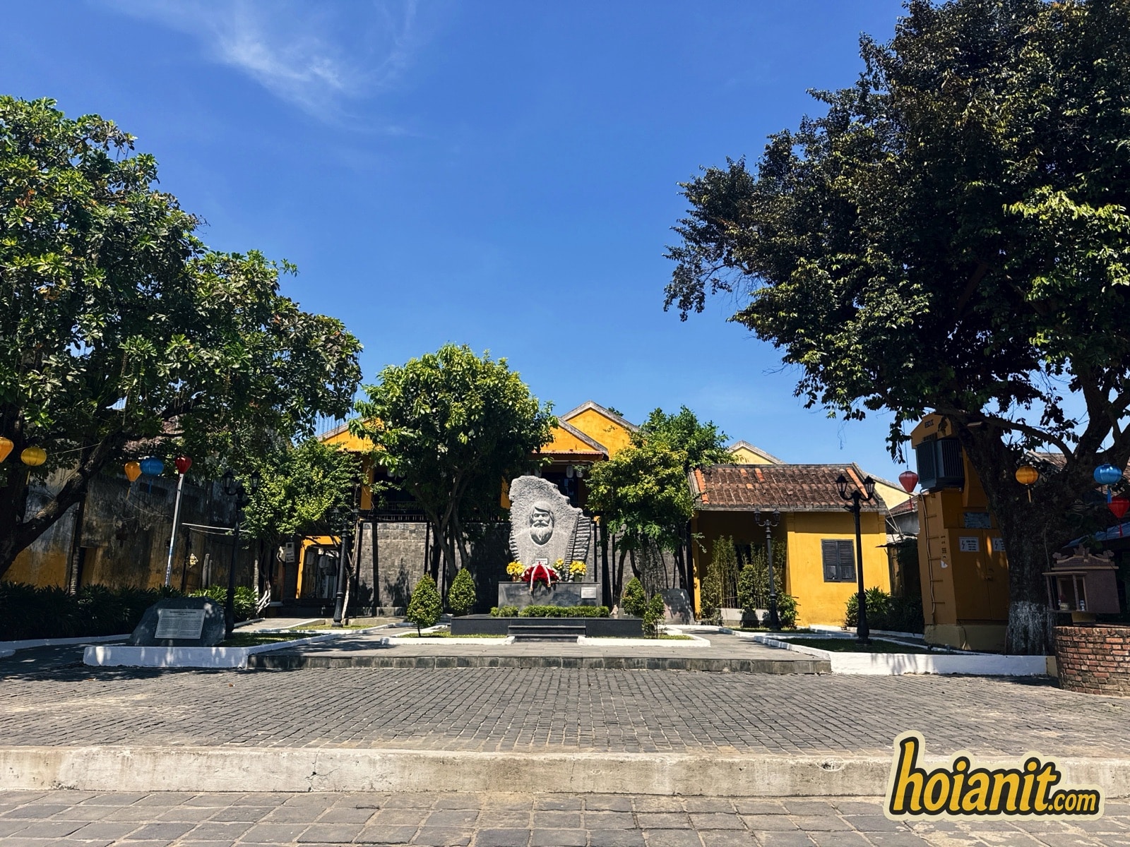 Kazik Hoi An park, wide view of the paved square, trees and the monument at the far end