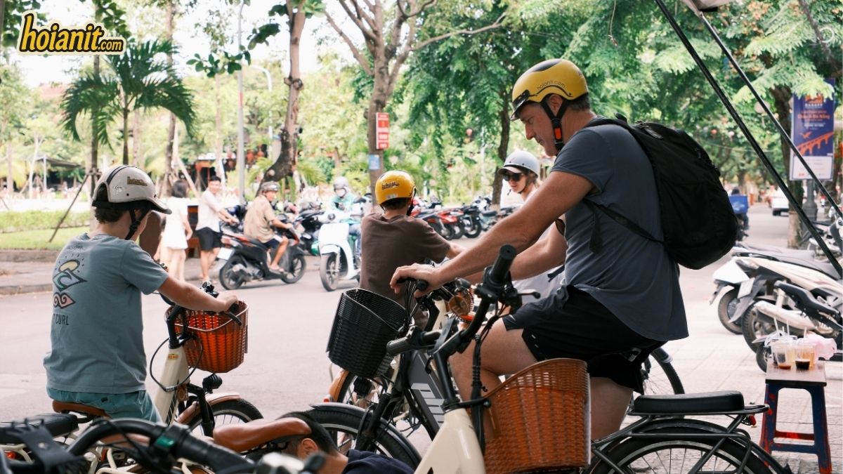 Group of travellers riding Anh Khoa rental bikes along a tree-lined street in Hoi An