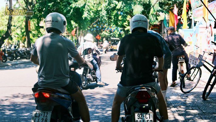 Tourists riding scooters on shaded Hoi An street rear view - motorbike rental Hoi An