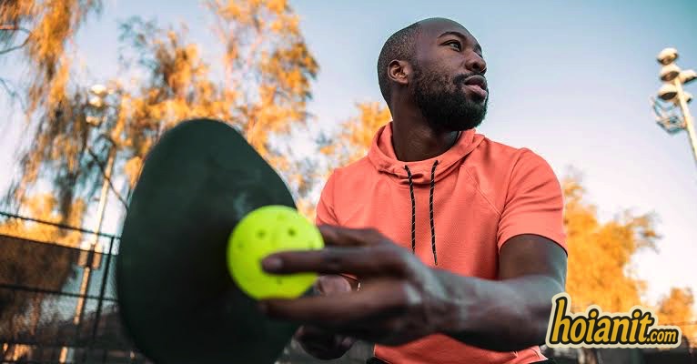 Close-up of a pickleball paddle and perforated plastic ball before a serve