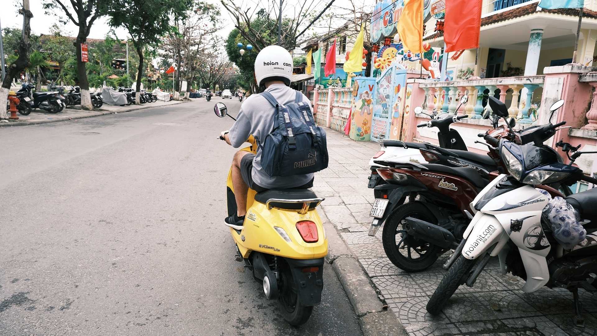 VinFast electric scooter range in Hoi An: a guest riding a yellow VinFast Evo along a town street